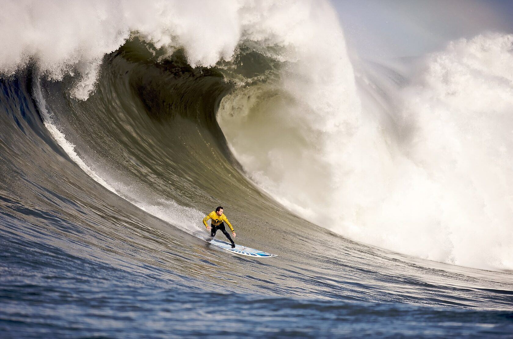 male surfer riding a blue surfboard at the base of a large wave